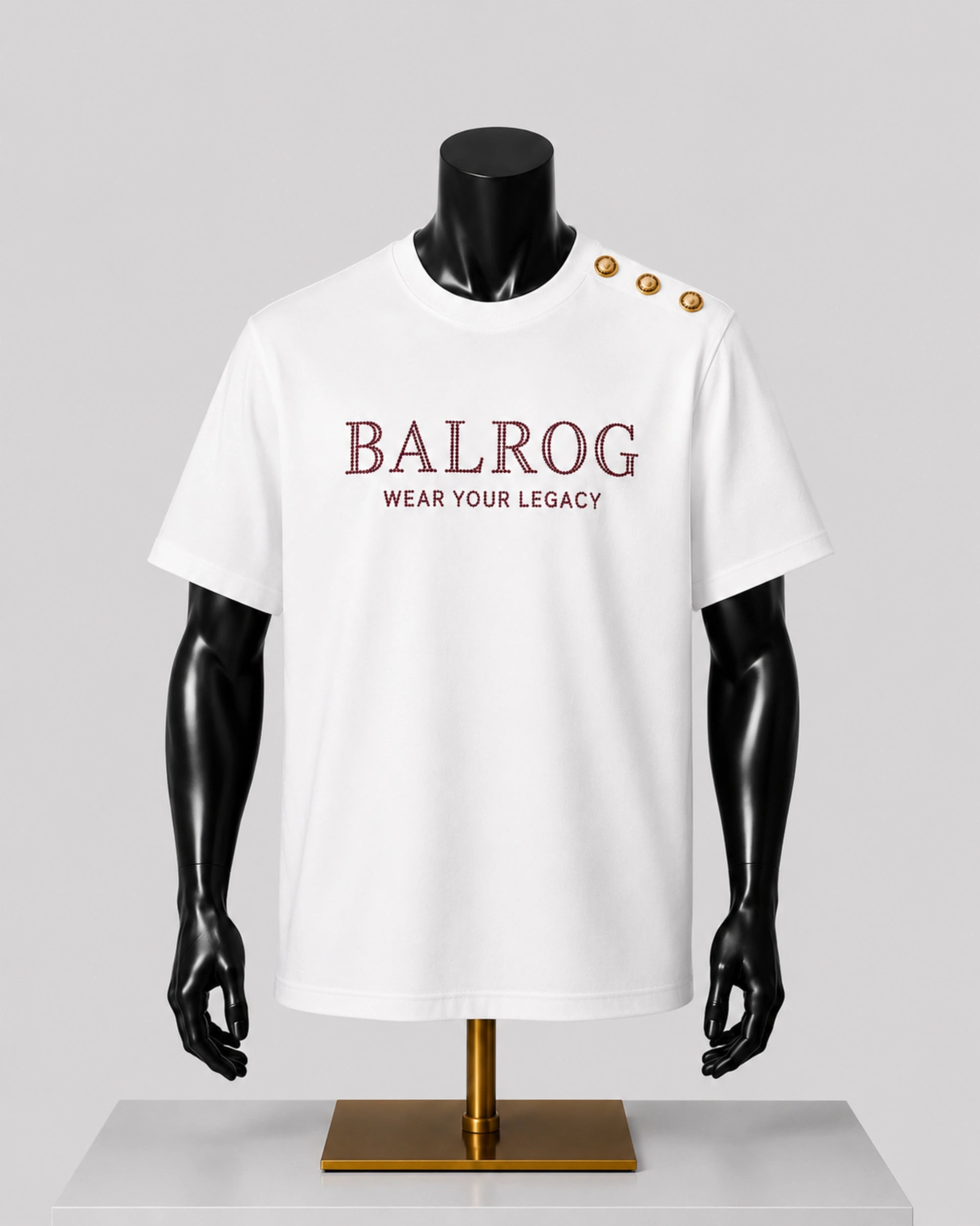 White short-sleeve T-shirt displayed on a black mannequin torso with gold buttons on the shoulder. The shirt has 'BALROG' and 'WEAR YOUR LEGACY' printed in burgundy across the chest, set against a light gray background.