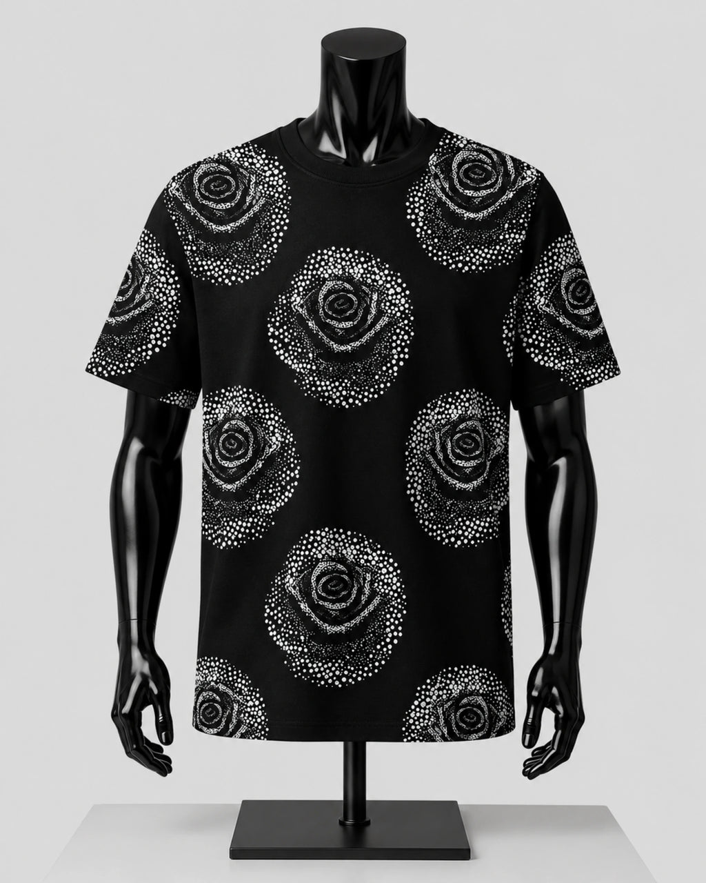 A black short-sleeve t-shirt with a white dotted rose pattern, displayed on a black mannequin against a light gray background.