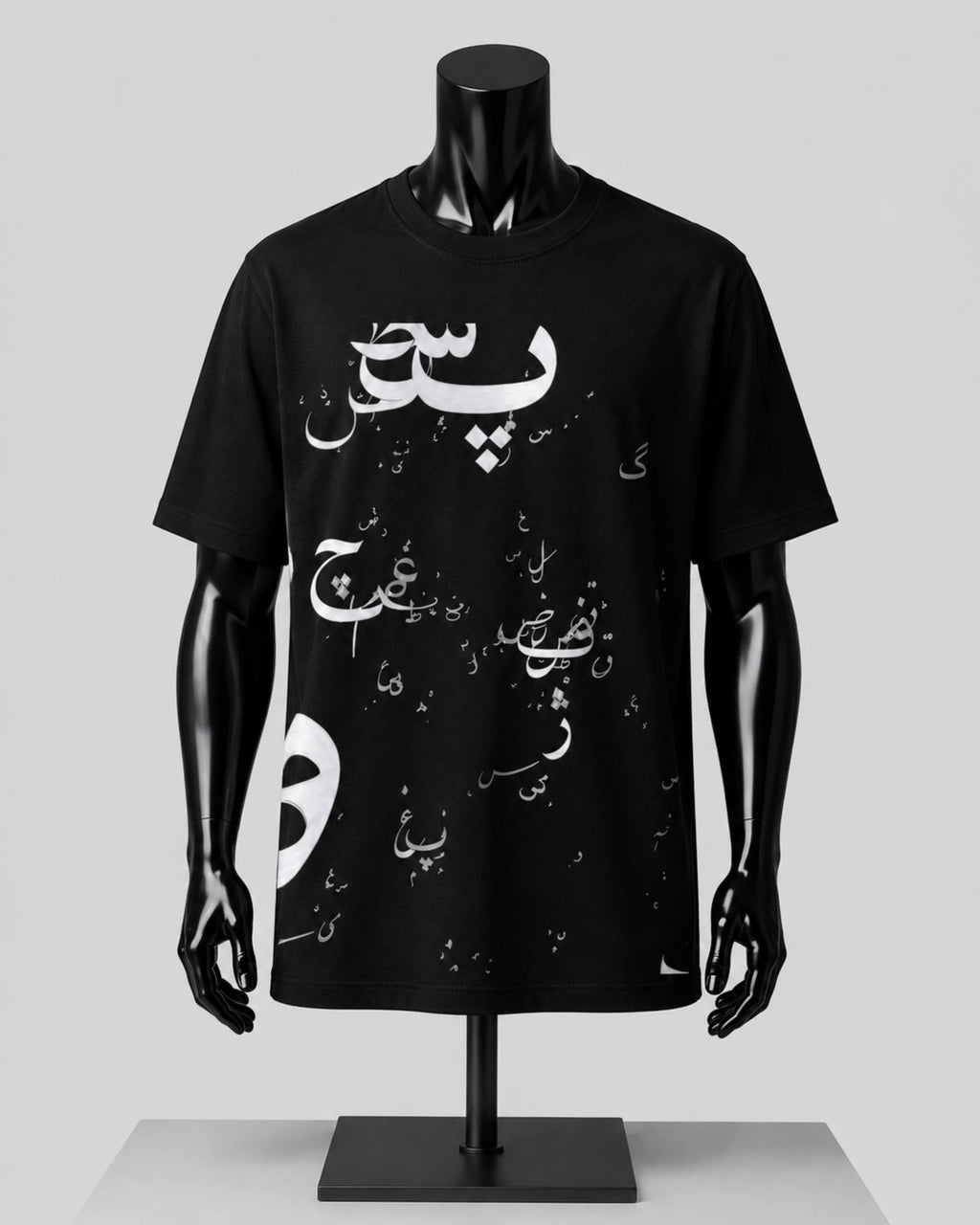 A black short-sleeve T-shirt displayed on a glossy black mannequin torso with arms and hands, featuring white Arabic calligraphy and small white graphic elements across the front, set against a light gray studio background.