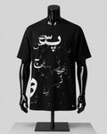 A black short-sleeve T-shirt displayed on a glossy black mannequin torso with arms and hands, featuring white Arabic calligraphy and small white graphic elements across the front, set against a light gray studio background.