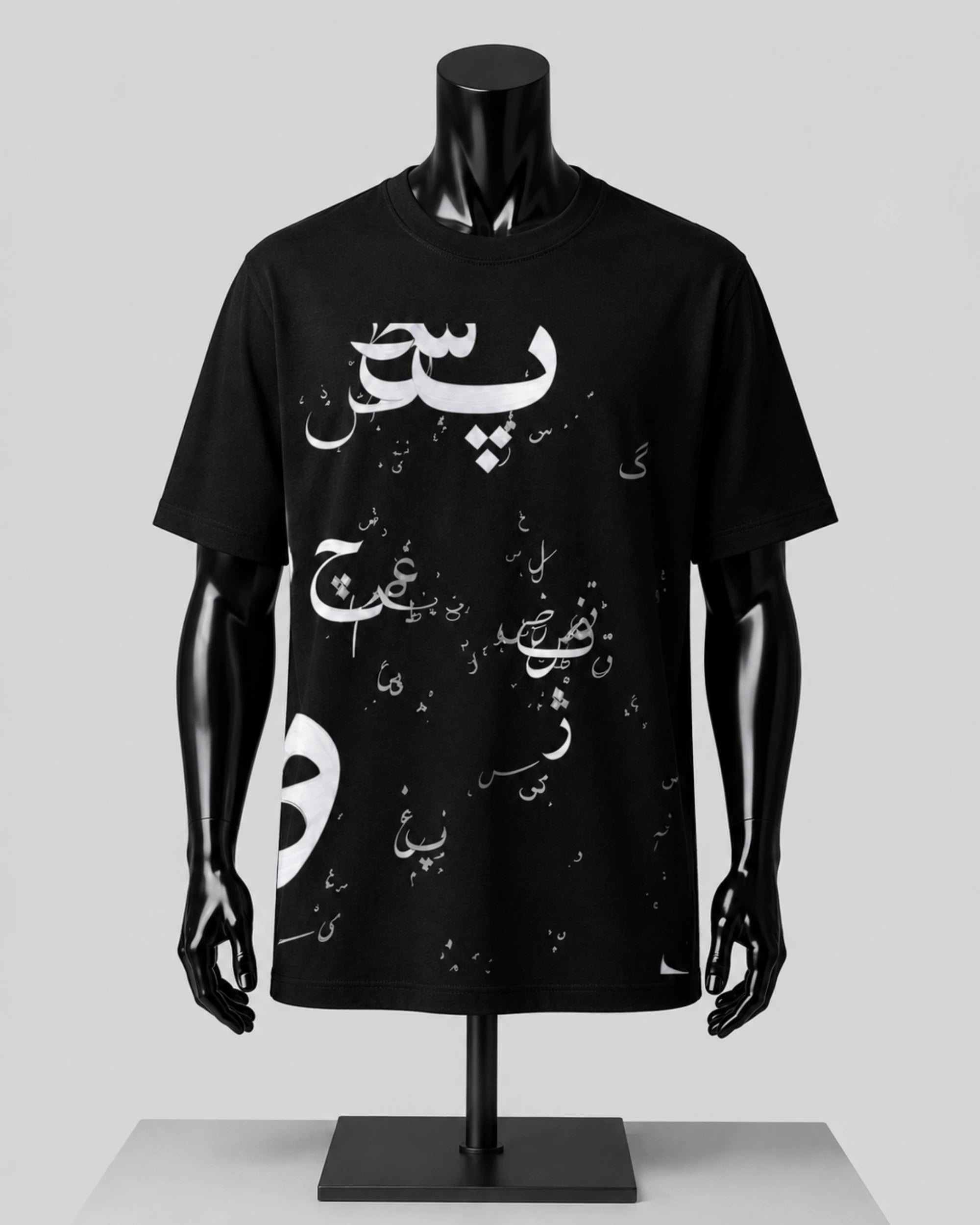 A black short-sleeve T-shirt displayed on a glossy black mannequin torso with arms and hands, featuring white Arabic calligraphy and small white graphic elements across the front, set against a light gray studio background.