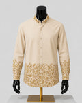 A men's long-sleeve button-up shirt in beige with a gold floral pattern along the collar, cuffs, and lower hem, displayed on a black mannequin torso with a gold stand against a light gray background.