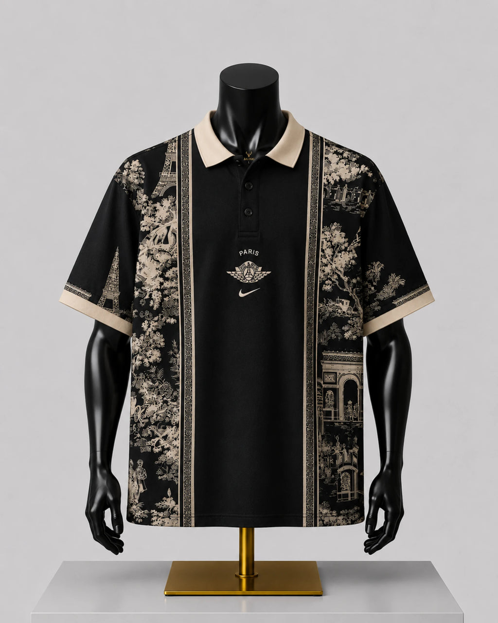 A black short-sleeve polo shirt with beige collar and sleeve trim, featuring beige scenic architectural and floral prints on the sides and a central gold-toned chest graphic, displayed on a black mannequin torso over a gold stand against a light gray background.