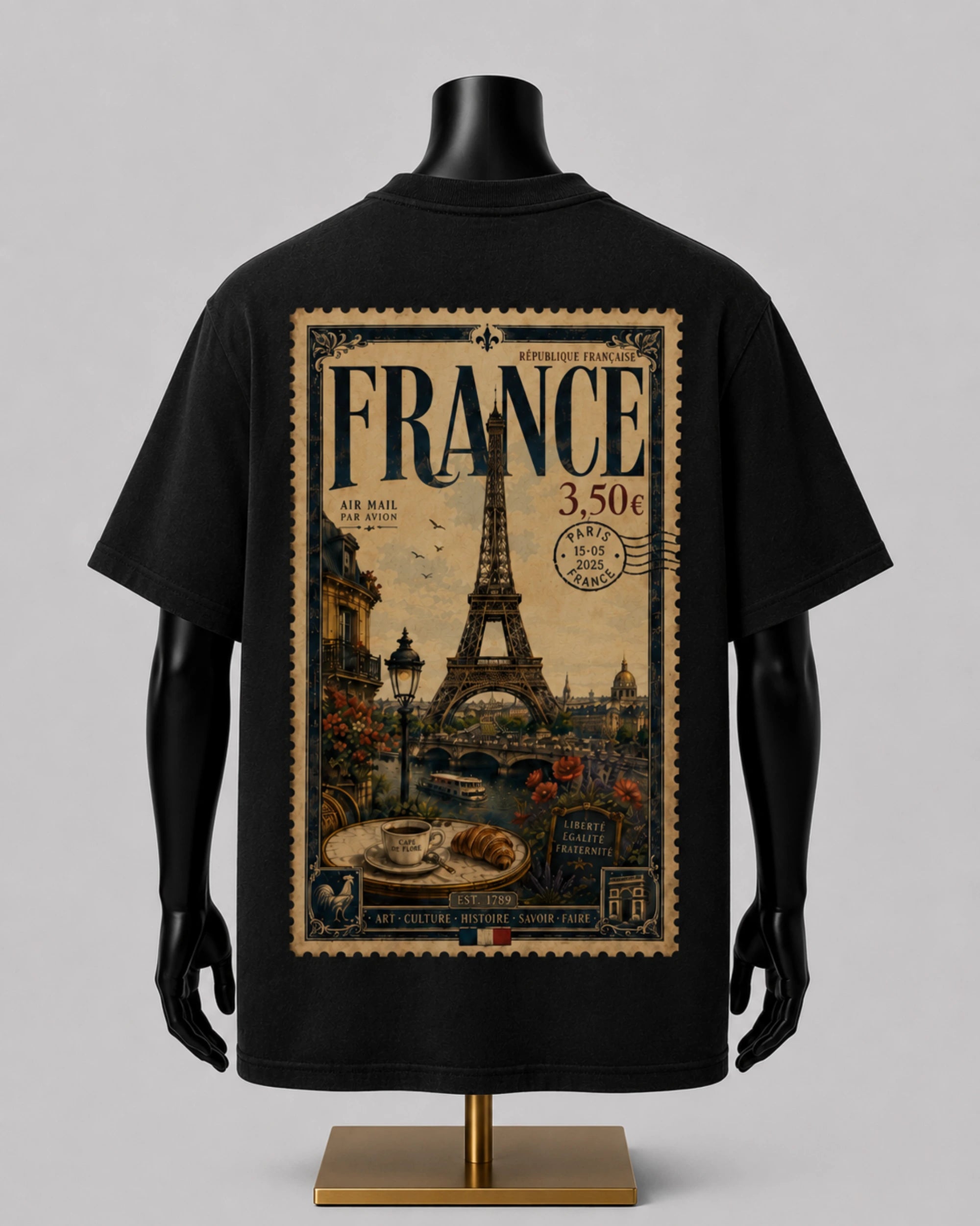 A black short-sleeve T-shirt displayed on a black mannequin torso with a gold stand, shown from the back. The shirt features a large vintage-style France postage stamp graphic with the Eiffel Tower, postmark details, and cafe imagery.