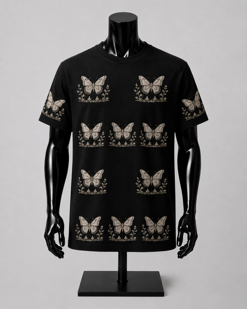A black short-sleeve crewneck t-shirt displayed on a black mannequin torso. The shirt features an all-over repeating pattern of beige butterflies with floral details underneath.