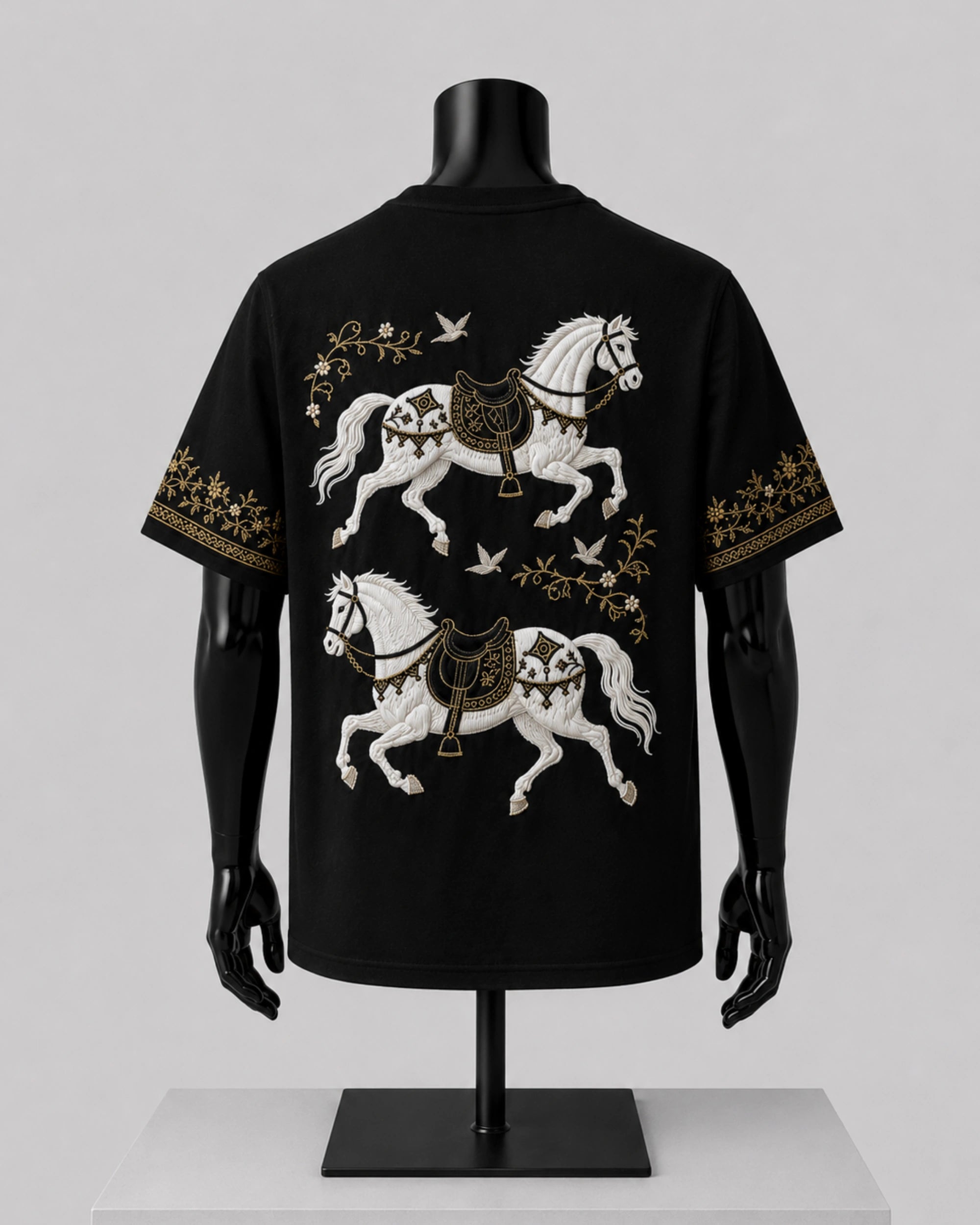 Black short-sleeve T-shirt displayed on a black mannequin torso, showing a large back print of two white horses with gold decorative details and small bird motifs.