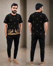 A man modeling a black short-sleeve t-shirt with gold peacock and floral embroidery, shown in front and back views against a neutral indoor backdrop.