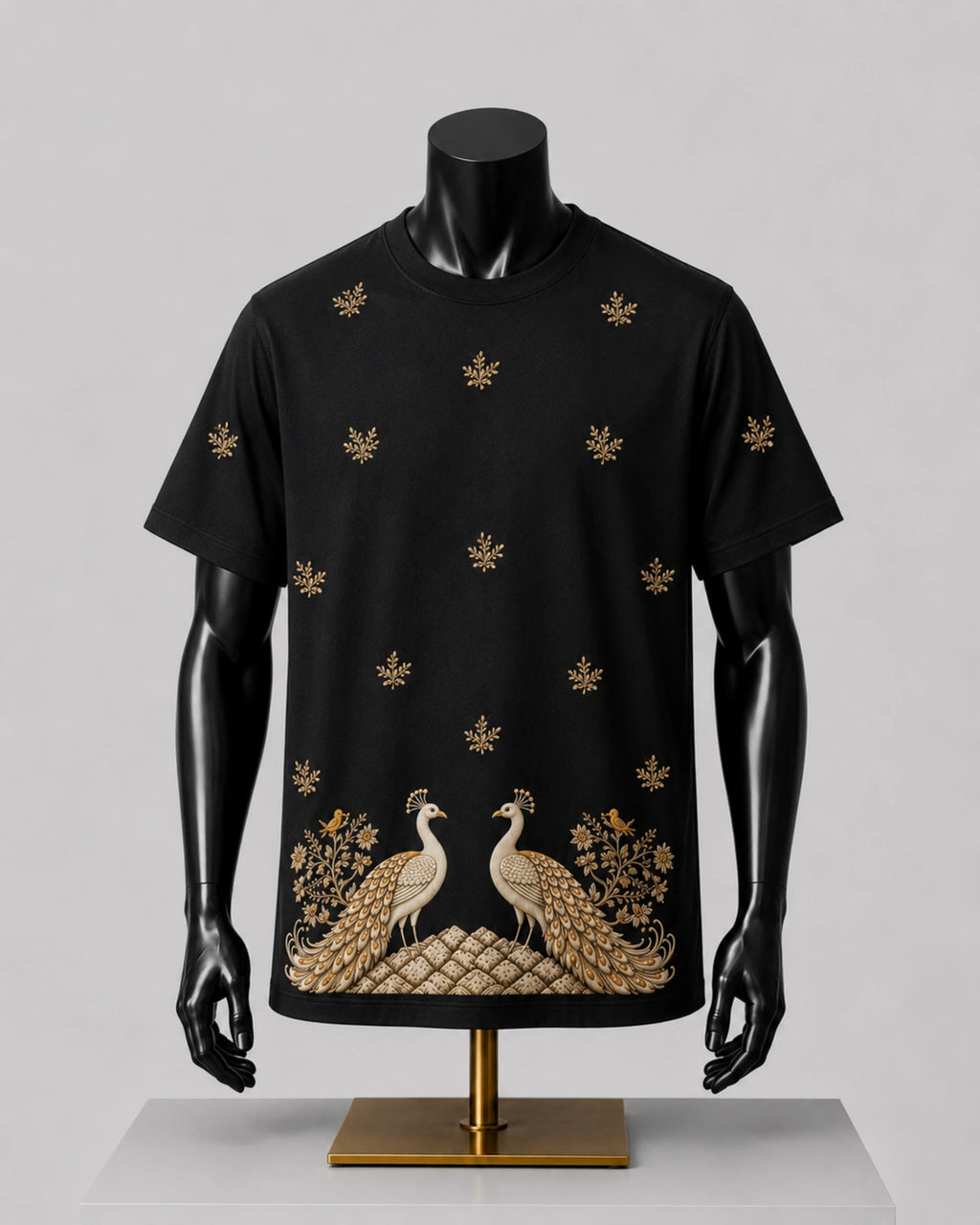 A black short-sleeve t-shirt displayed on a black mannequin torso, featuring gold embroidered peacocks and floral motifs along the bottom hem and scattered across the chest.