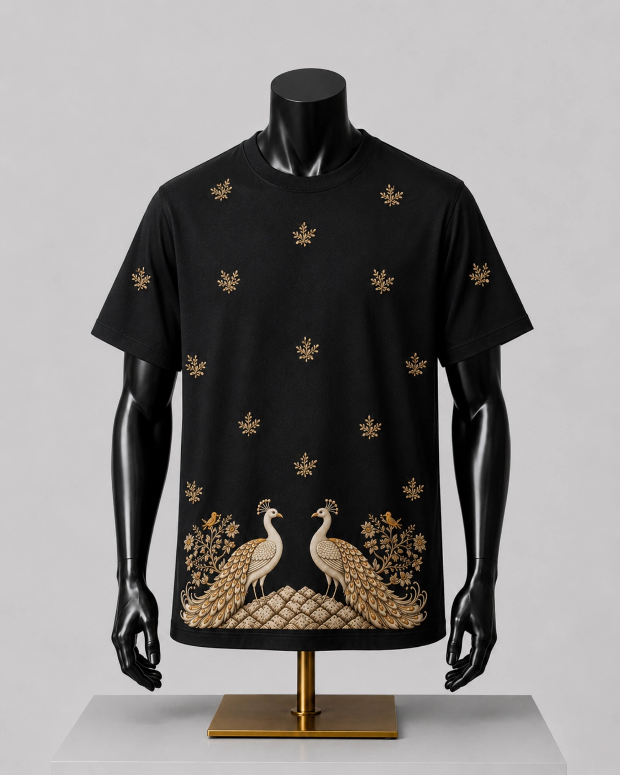 A black short-sleeve t-shirt displayed on a black mannequin torso, featuring gold embroidered peacocks and floral motifs along the bottom hem and scattered across the chest.
