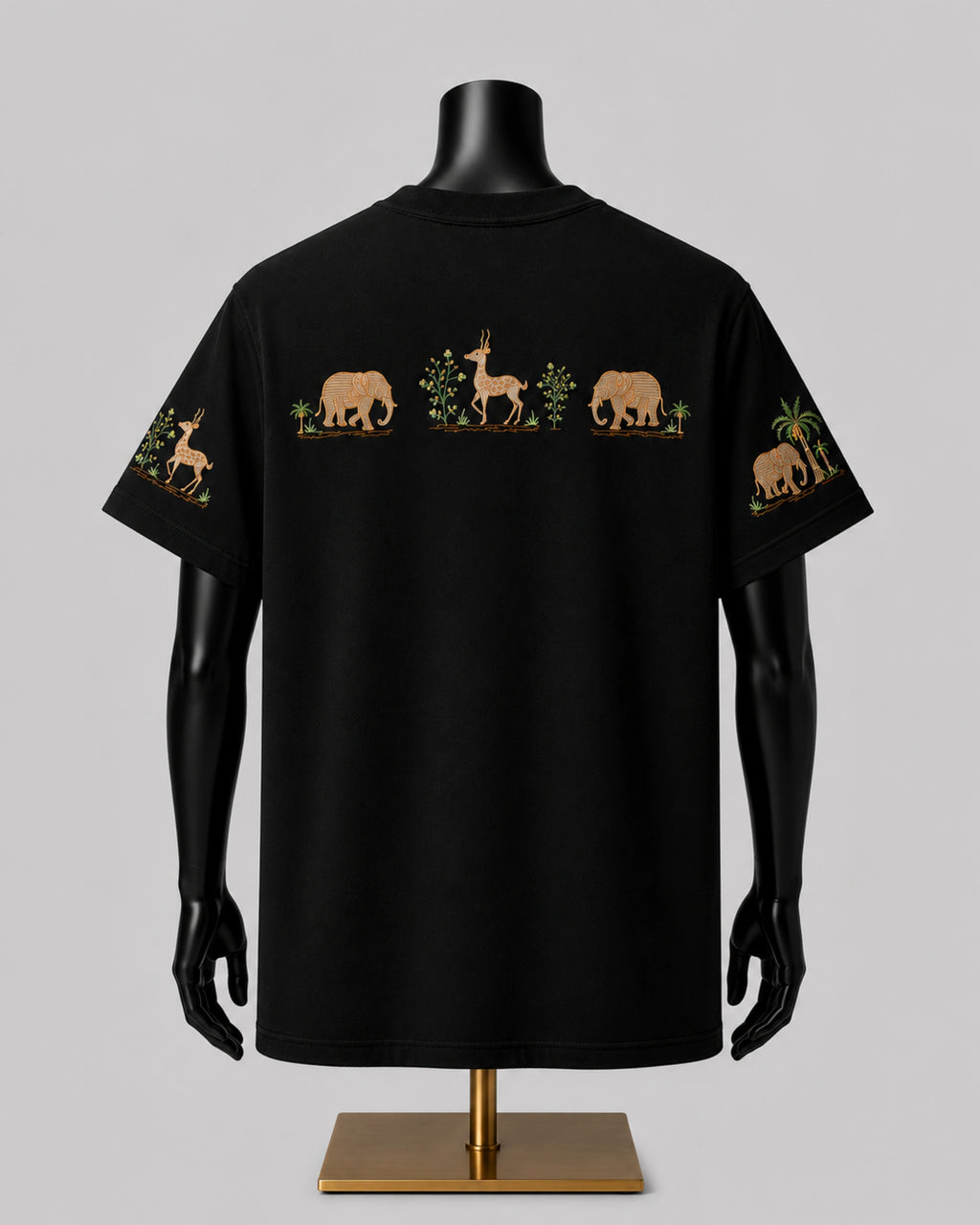 Black short-sleeve T-shirt displayed on a black mannequin torso with a gold stand, showing a safari animal print across the back with elephants, a gazelle, and palm trees, plus matching prints on both sleeves, against a solid gray background.