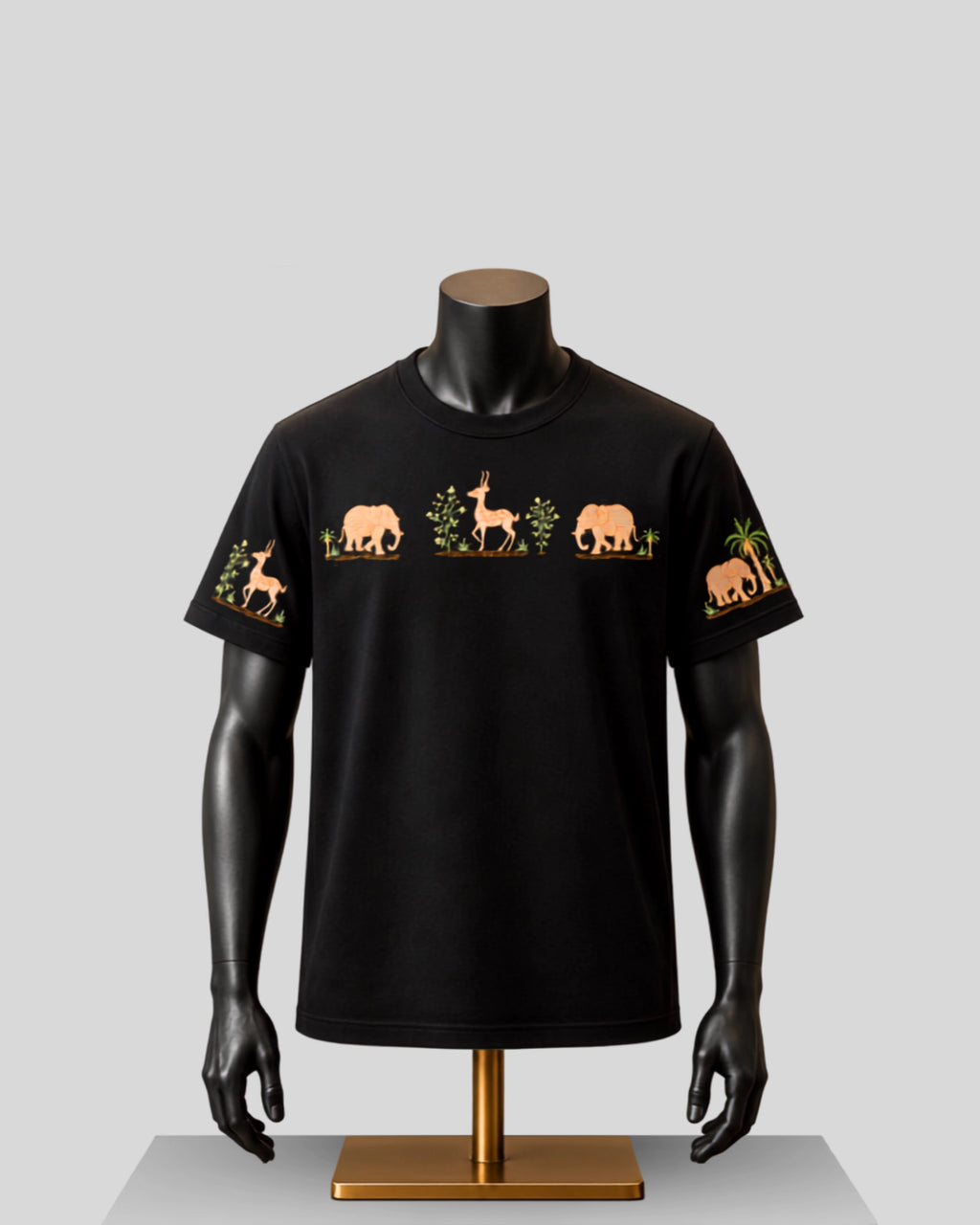 A black short-sleeve crewneck t-shirt displayed on a black mannequin torso with a gold stand, featuring embroidered safari animal motifs including an elephant, gazelle, and palm tree on the chest and sleeves.
