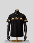 A black short-sleeve crewneck t-shirt displayed on a black mannequin torso with a gold stand, featuring embroidered safari animal motifs including an elephant, gazelle, and palm tree on the chest and sleeves.