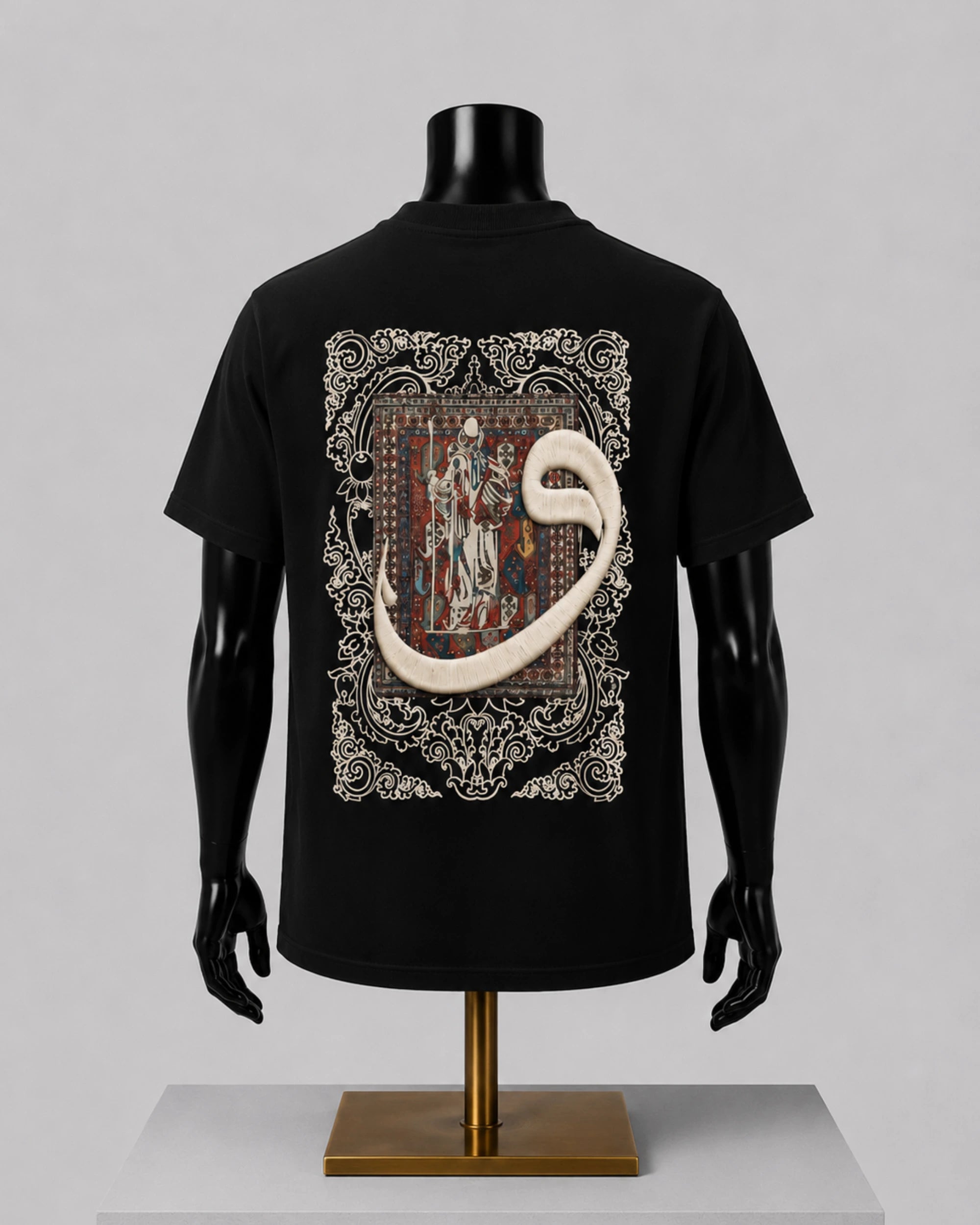 A black short-sleeve T-shirt displayed on a black mannequin torso with a gold stand, shown from the back against a light gray studio background. The shirt features a large ornate graphic print with a beige scroll motif over a detailed medieval-style illustration.